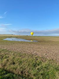 Hei&szlig;luftballon in der Luft spiegelt sich in einer Wasserp&uuml;tze, die sich auf einem abgeernteten Feld befindet.